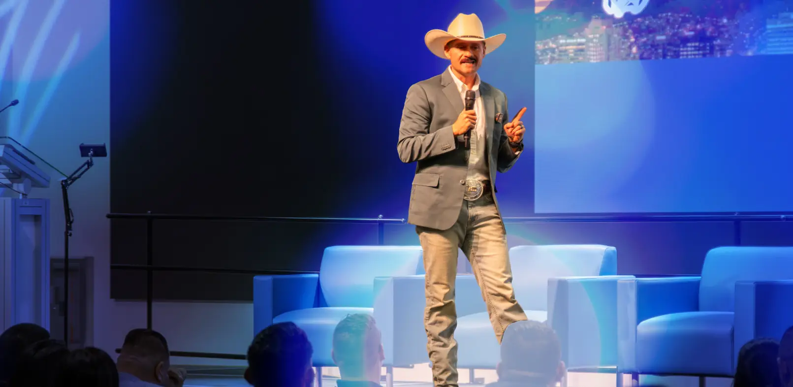 Marcos Ramírez hablando con micrófono en un escenario iluminado de azul